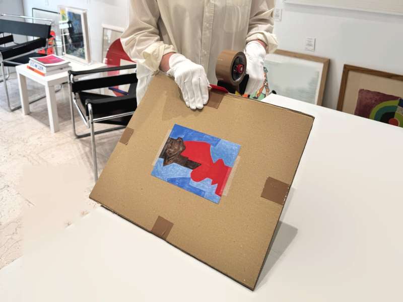 Carton plat refermé sur l’œuvre, scotché sur les bords, avec une reproduction de l’œuvre collée sur le dessus