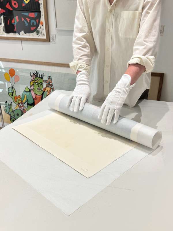 Estampe roulée entre des feuilles de papier de soie par une personne portant des gants de coton