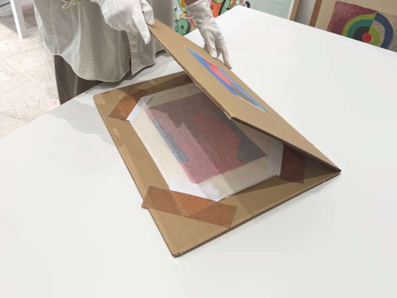 Estampe maintenue sur le carton par des coins de protection en papier fixés au ruban adhésif, avant fermeture du carton